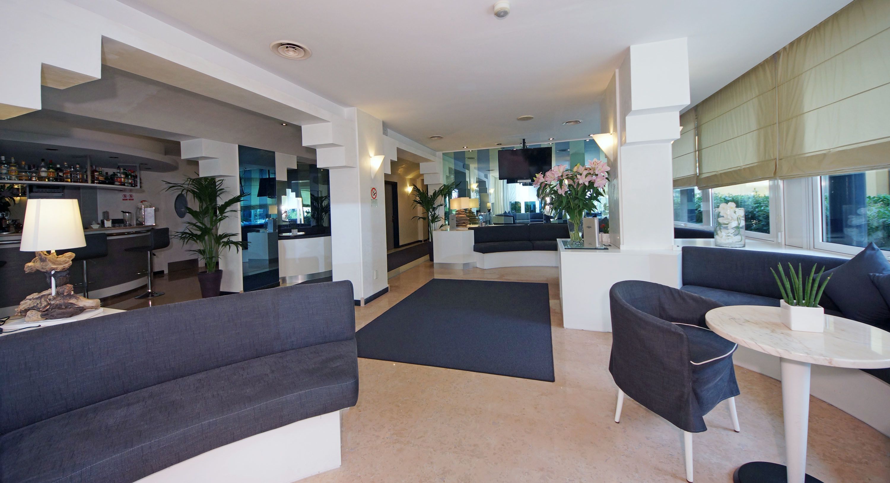 Um hall de hotel moderno com área de bar, espaços para sentar e uma grande janela com vista.
