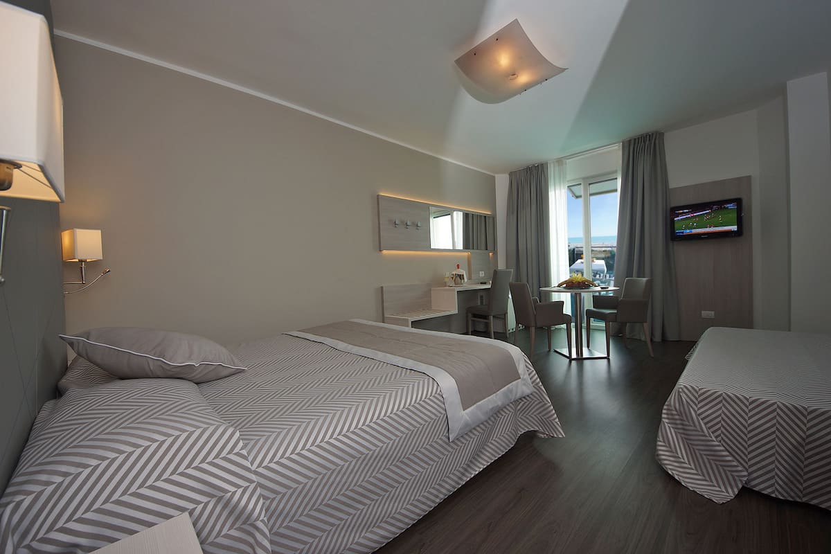 A hotel room with a large bed, a desk, a chair, a TV, and a view of the city.
