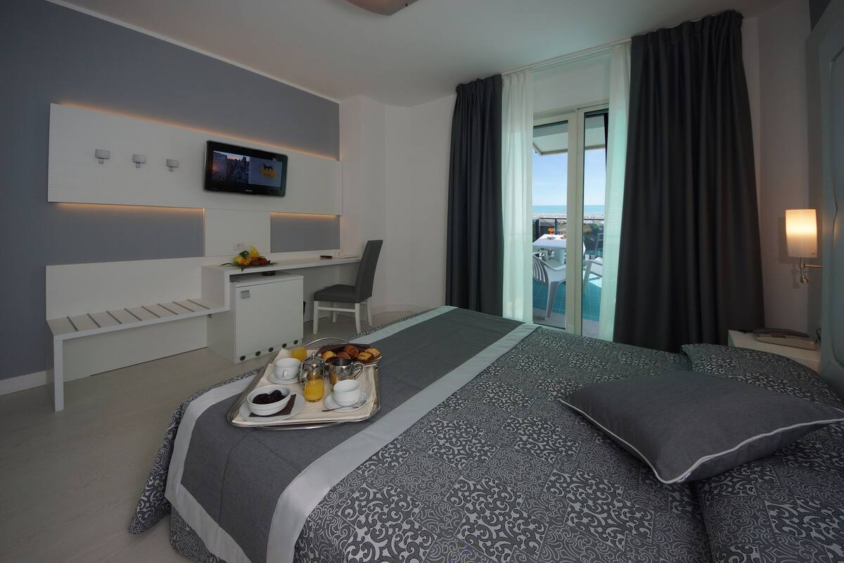 A modern hotel room with a bed, a desk, a TV, and a balcony with curtains.