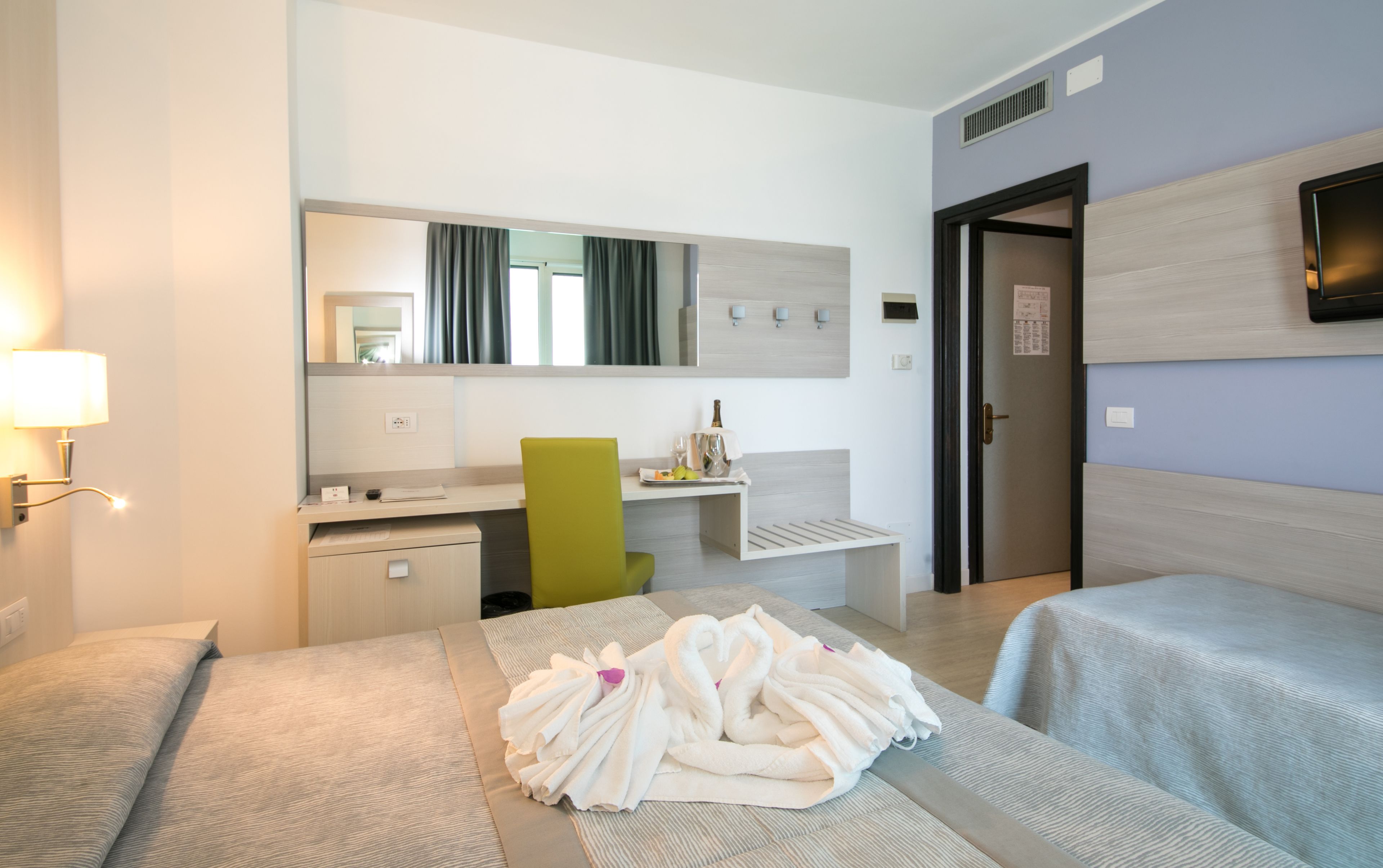 Una camera d'albergo con un letto, una scrivania, una sedia, una TV e l'ingresso del bagno.
