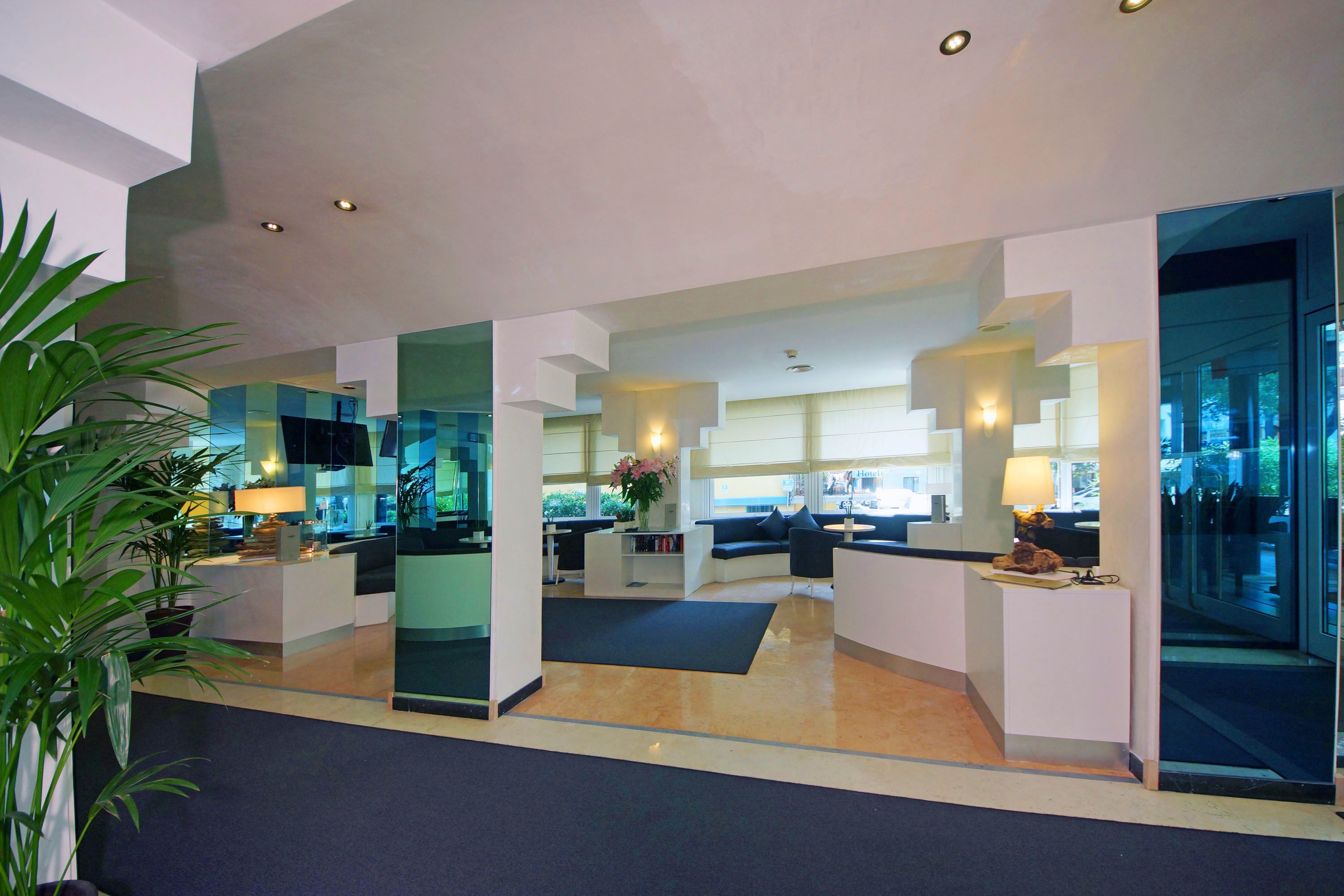 A modern hotel lobby with a reception desk, seating area, and large windows.