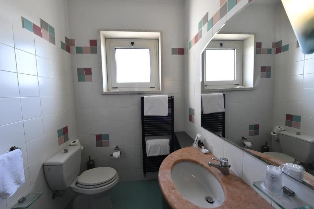Ein kleines Badezimmer mit Toilette, Waschbecken und einem Fenster über der Toilette.