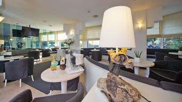 A modern hotel lobby with seating areas, a bar, and a large window offering a view of the city.