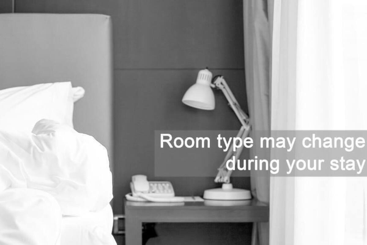 A hotel room with a bed, a nightstand with a lamp, and a telephone. Text indicates room type may change during the stay.
