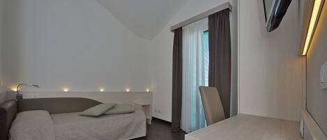 Una habitación de hotel moderna con una cama, un escritorio, una silla, un televisor montado en la pared y una ventana con cortinas.