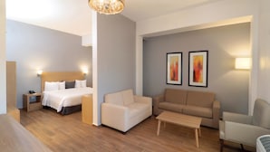 A modern hotel room with a wooden floor, a bed with a headboard, a sofa, a coffee table, and two wall-mounted lamps. - Bluu Hotel (Frontera)