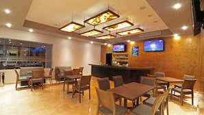 A restaurant with wooden tables and chairs, a bar area, and two televisions on the wall. - Bluu Hotel (Frontera)