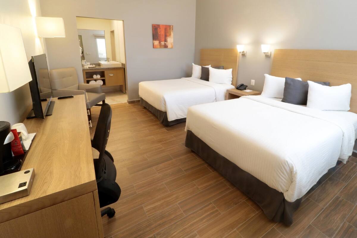 A hotel room with two beds, a desk with a computer, a chair, a desk lamp, a telephone, and a mirror.
