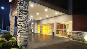 A modern building entrance with a stone pillar, glass doors, and a well-lit interior. - Bluu Hotel (Frontera)