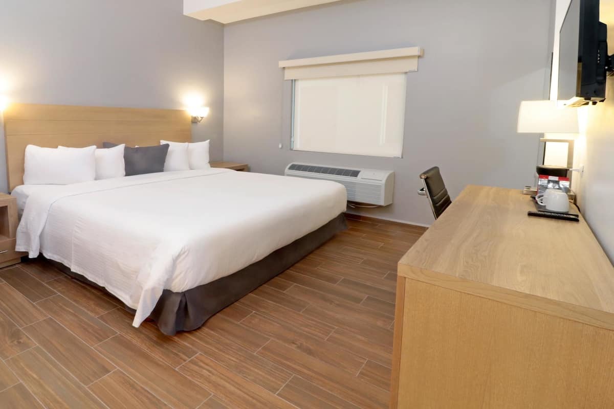 A hotel room with a large bed, bedside tables, a desk, and a wall-mounted TV.