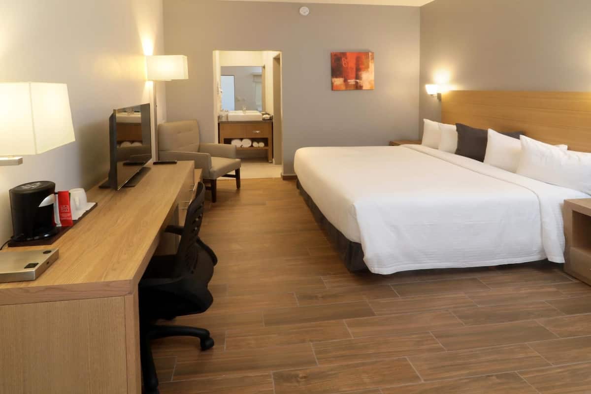 A hotel room with a large bed, bedside tables, a desk with a chair, a mirror, and a bathroom visible through an open door.