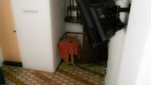 A narrow hallway with a tiled floor, a small wooden table with a red tablecloth, and a door with a metal handle. - El Dorado Residencial (Lima)
