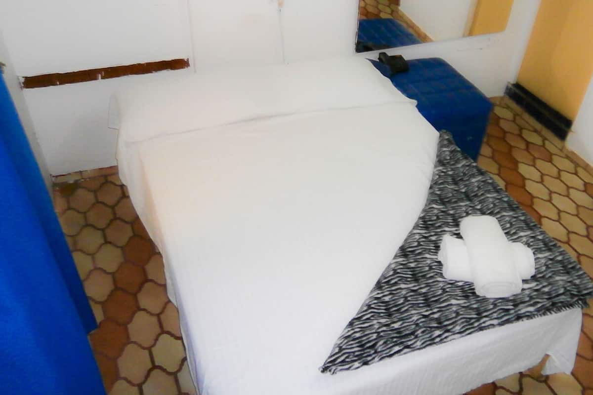 Ein kleines, sauberes Zimmer mit einem Bett, einer Sitzbank und einem Teppich mit Muster.