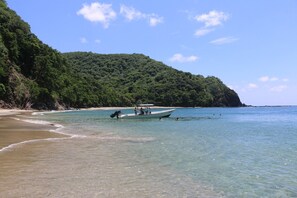 A boat on a clear beach with a forested hill in the background. - C & K Apartments (Castara)
