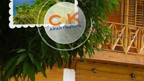 A wooden balcony with a railing, a sign for C&K Apartments, and some greenery. - C & K Apartments (Castara)