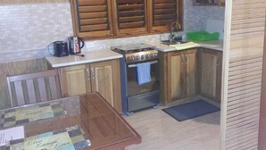 A compact kitchen with wooden cabinets, a gas stove, a microwave, and a small dining table with a placemat. - C & K Apartments (Castara)