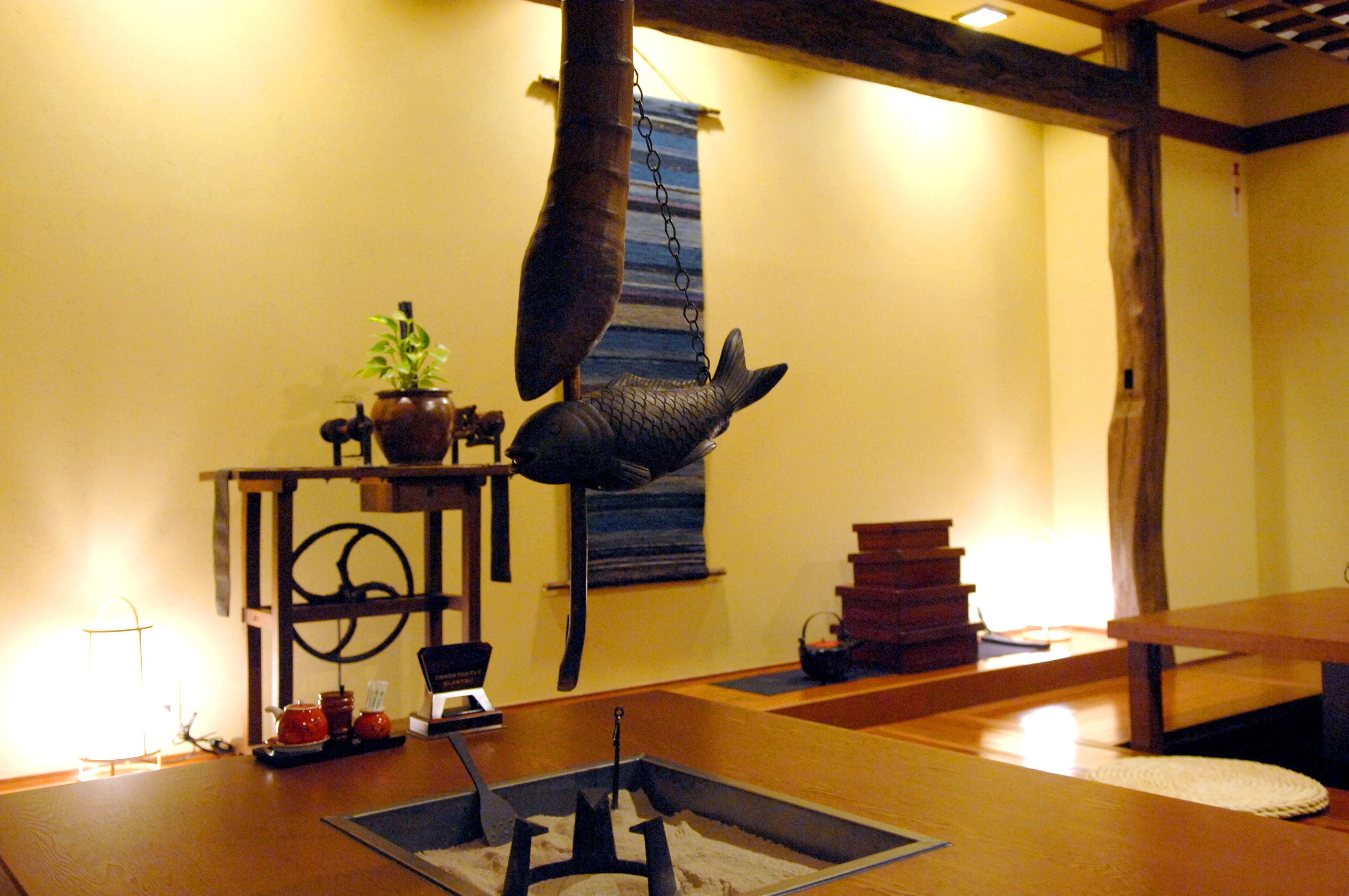 A traditional Japanese room with tatami flooring, a hanging fish sculpture, and a small table with a teapot and cups.