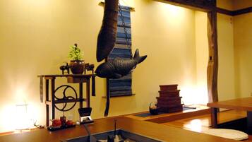 A traditional Japanese room with tatami flooring, a hanging fish sculpture, and a small table with a teapot and cups.
