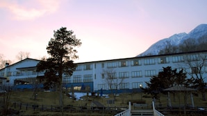 A multi-story building with a flat roof and large windows, surrounded by a landscaped area with trees and a wooden deck. - Sapporo’s Secret Onsen Sanctuary Marukoma Onsen Ryokan (Chitose)