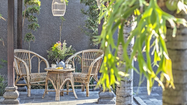A bamboo chair and table set under a pergola with hanging birdcages, surrounded by greenery. - Villa Kedis (Canggu)