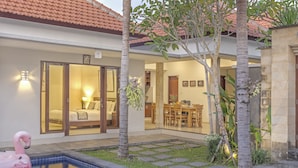 A residential property with a swimming pool, a dining area, and a bedroom with a large window. - Villa Kedis (Canggu)