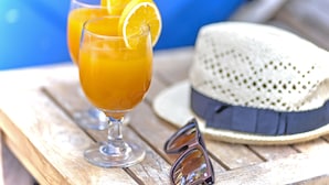 Two glasses of orange juice with lemon slices, a straw, a white hat, and a pair of sunglasses on a wooden table. - Villa Kedis (Canggu)