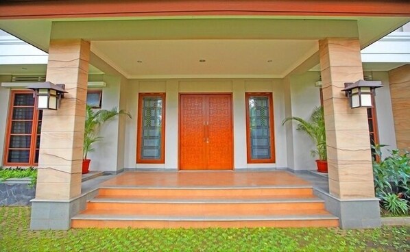 A building entrance with a wooden door, two windows with decorative glass, and a covered porch with steps. - Rumah Aca (Bandung)