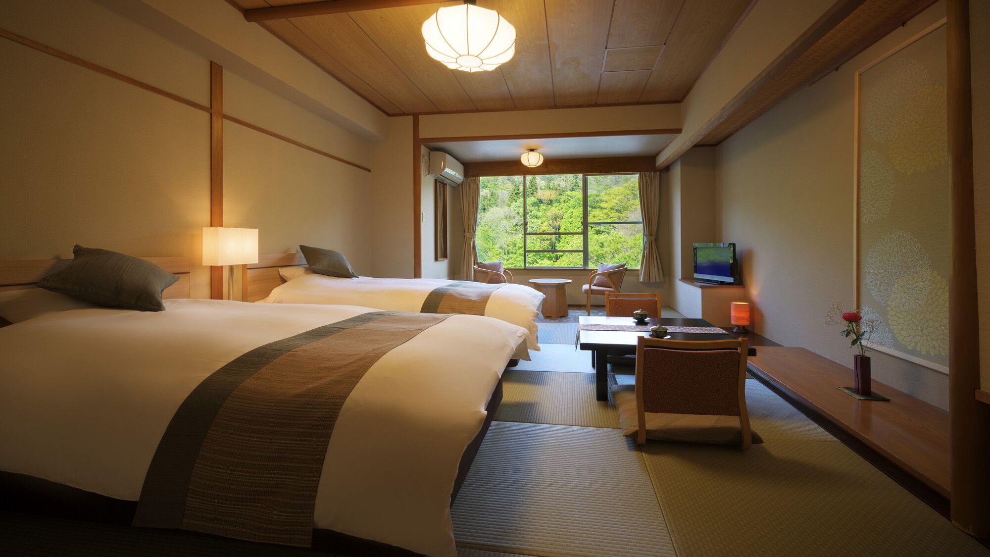 Habitación de hotel con dos camas, una mesa de comedor, sillas, televisor y ventana con vista a áreas verdes.