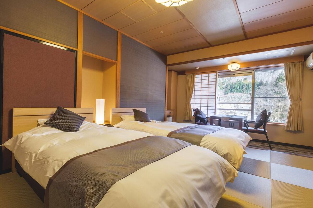 A hotel room with two beds, a desk, and a window with curtains.