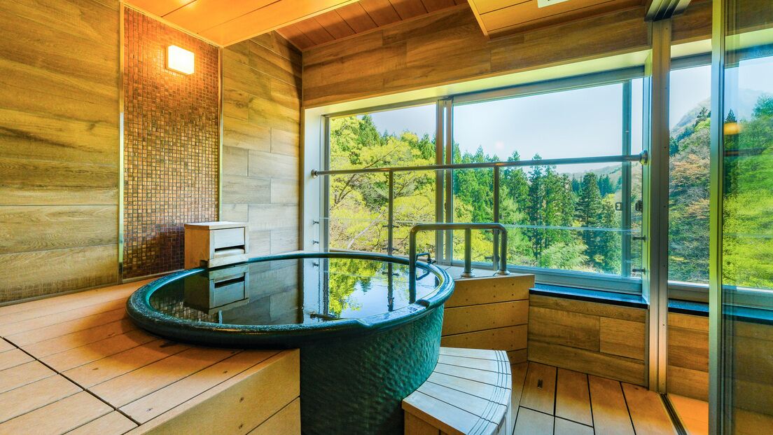 Interior de madera con una bañera de hidromasaje acristalada y vistas a un bosque a través de amplios ventanales.