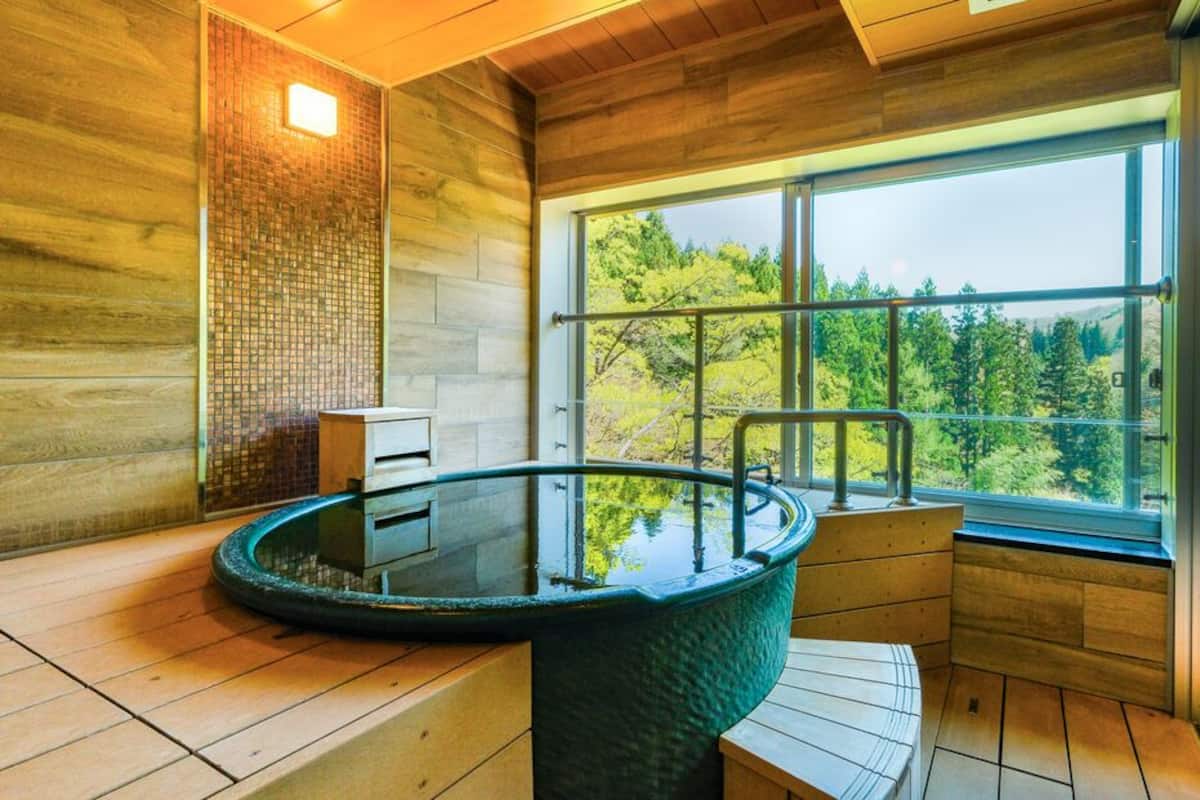 A wooden interior with a glass-enclosed hot tub and a view of a forest through large windows.