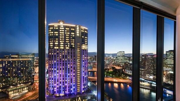 Un hotel de gran altura con un llamativo letrero que dice "Crown", amplias ventanas y vistas de un paisaje urbano y una masa de agua por la noche.