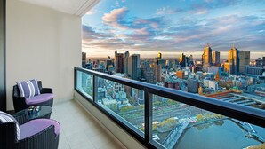 Un balcón con vista a la ciudad, muebles de mimbre y una mesa de vidrio.