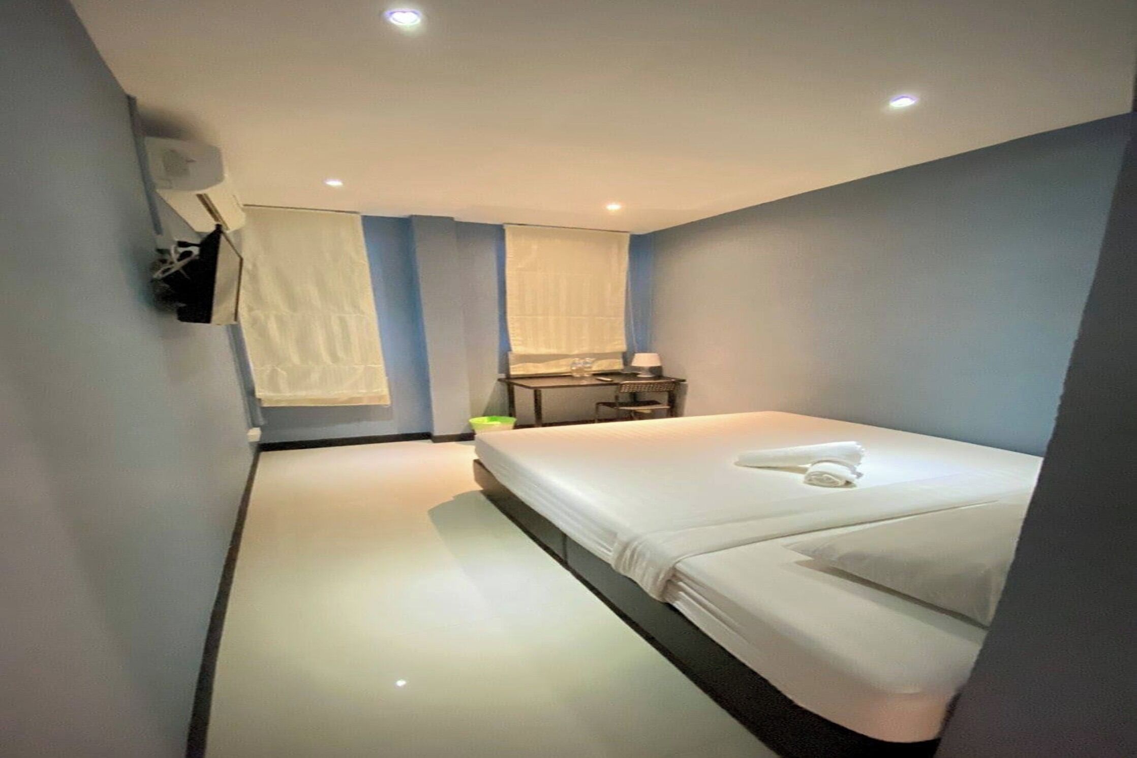 Quarto de hotel com cama, escrivaninha, cadeira, espelho e janela com cortinas.
