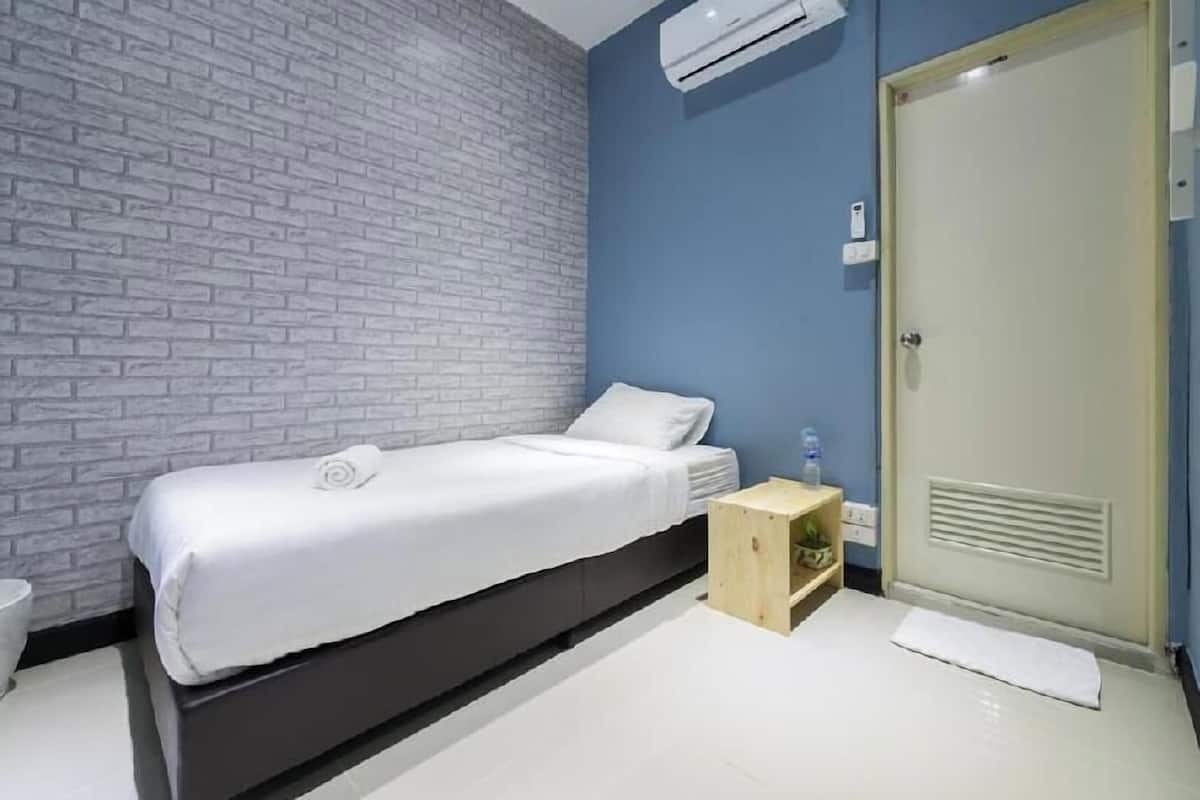 A modern room with a bed, a small wooden side table, a white trash bin, and a door with a light switch.