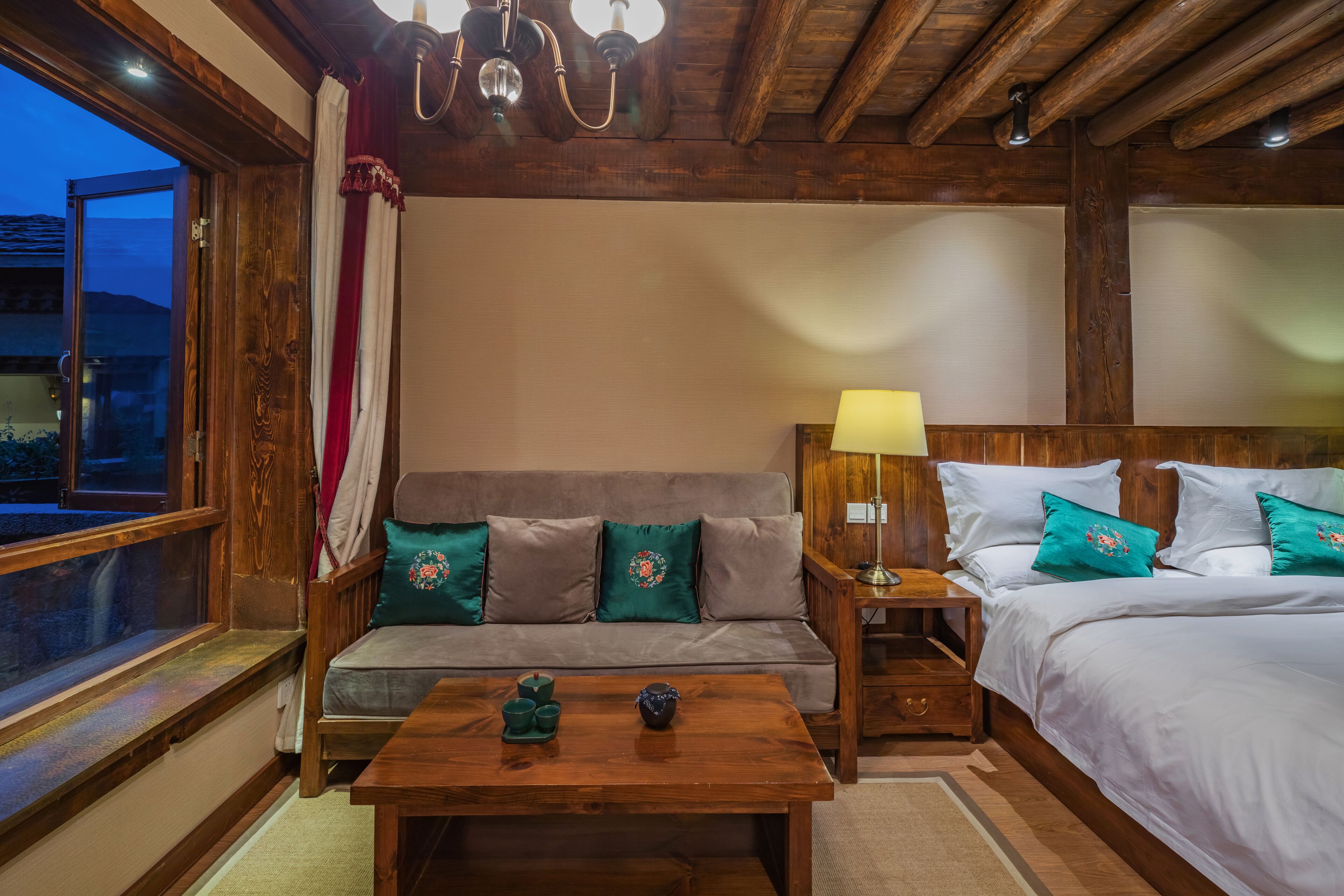 Ein gemütliches Zimmer mit Holzbalkendecke, einer Couch mit grünen Kissen, einem Bett mit weißer Bettwäsche und einem Nachttisch mit Lampe.