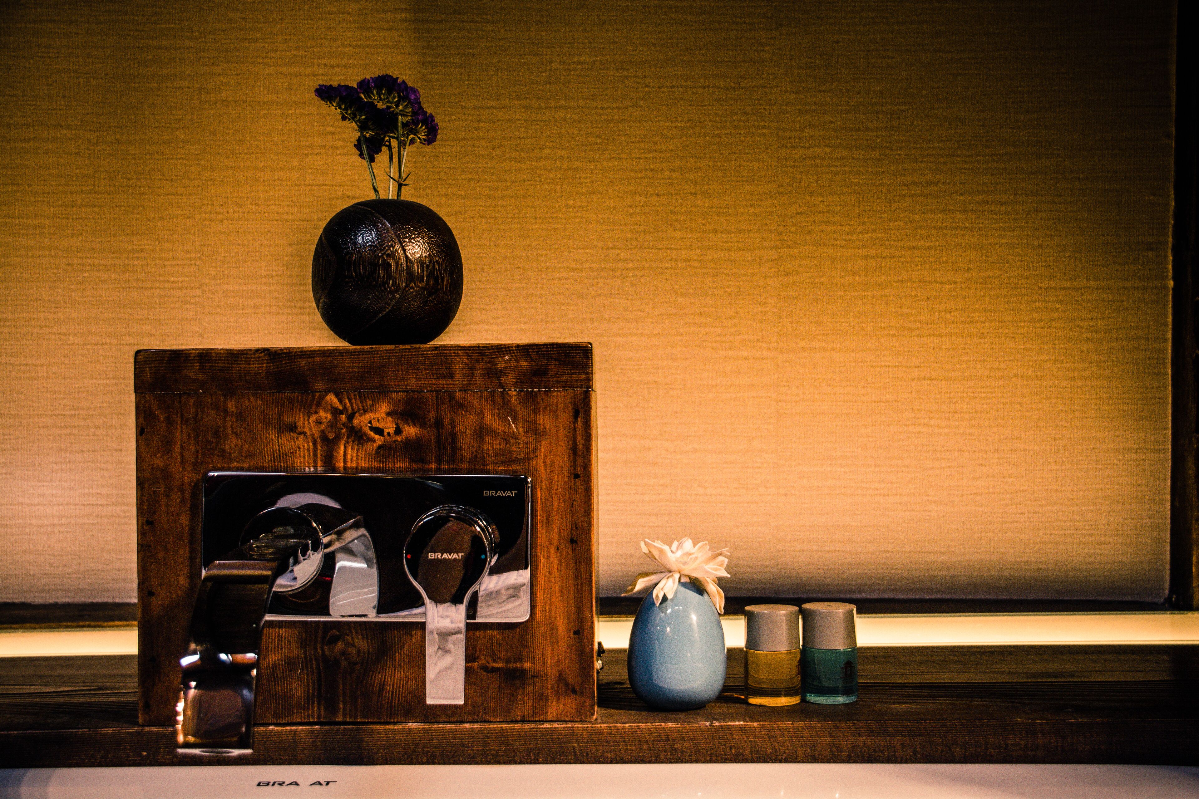 A wooden vanity with a mirror, a vase with flowers, and toiletries.