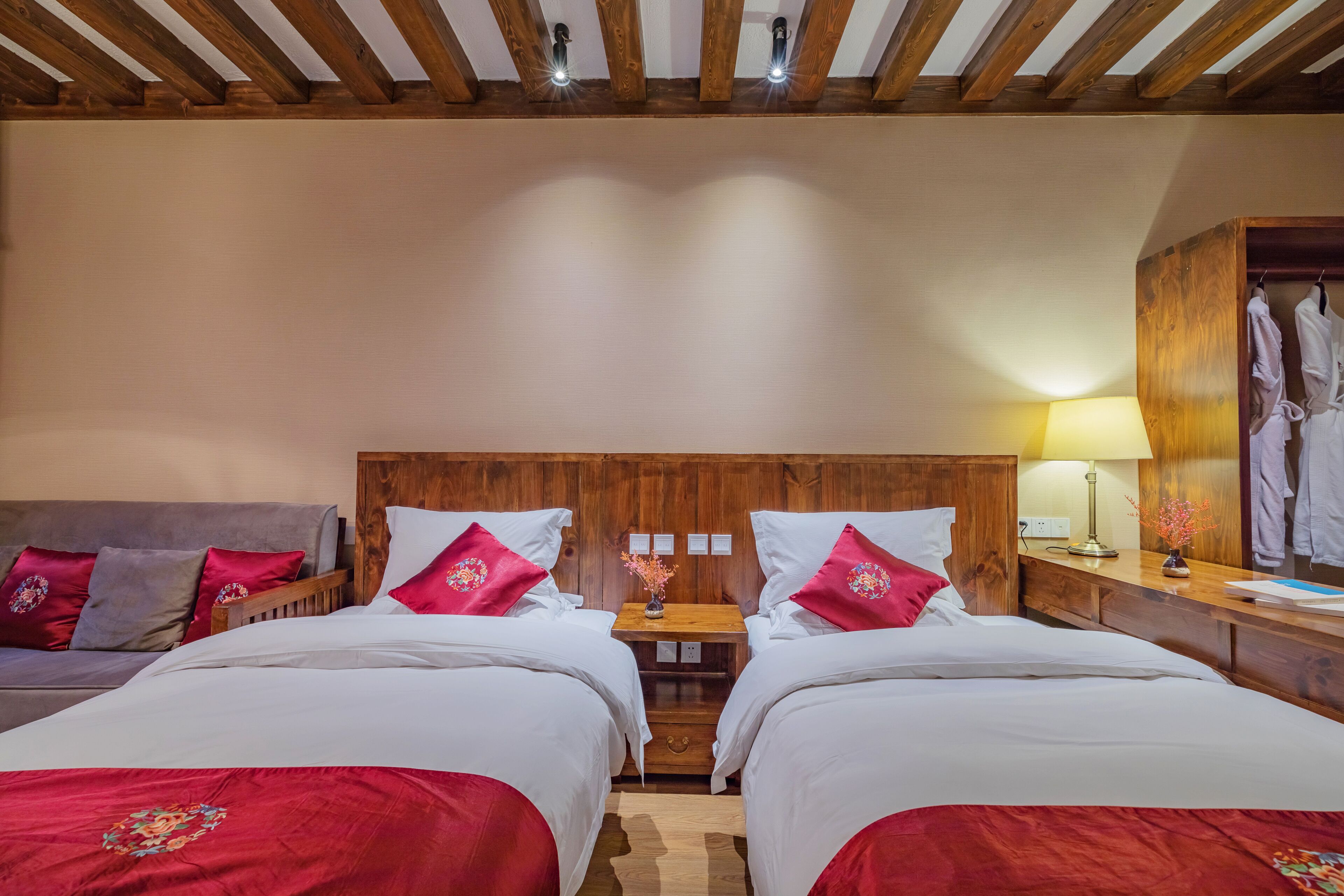 A hotel room with two beds, a wooden headboard, a nightstand with a lamp, and a wardrobe.