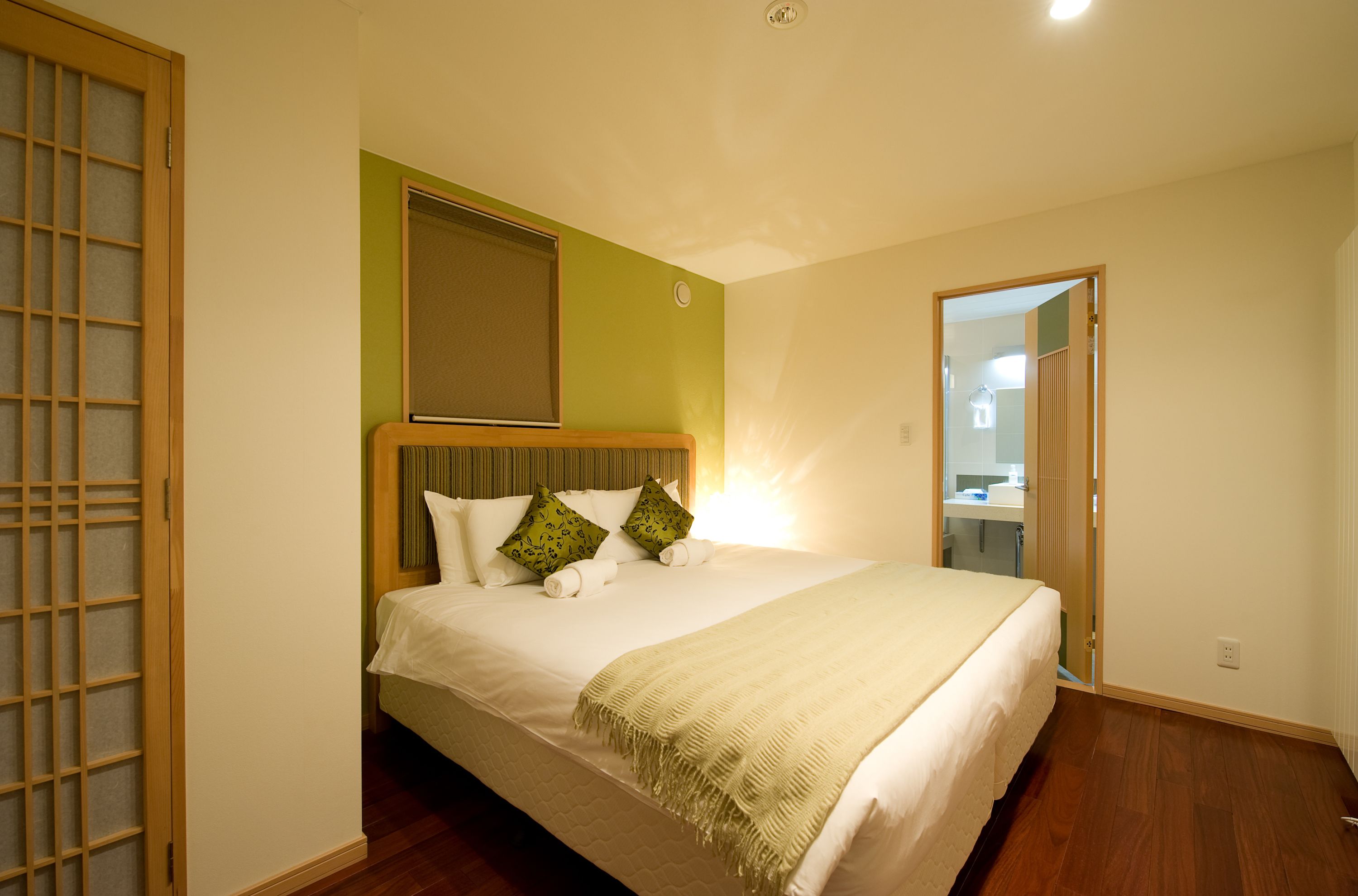 A neatly made bed with pillows and a blanket, a wooden headboard, and a green accent wall.