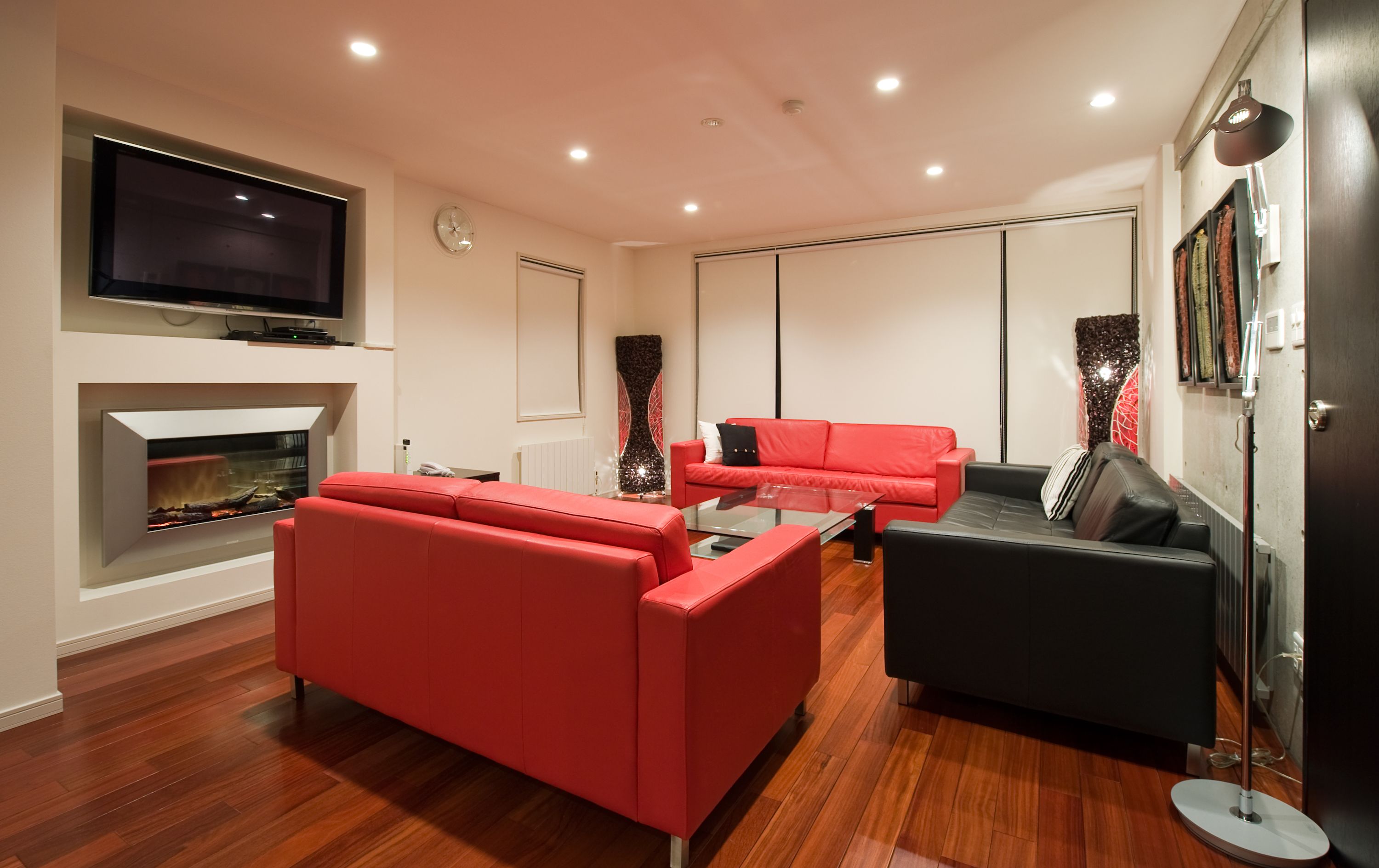 Una sala de estar moderna con chimenea, sofás rojos y negros, un televisor de pantalla plana y un gran jarrón decorativo.