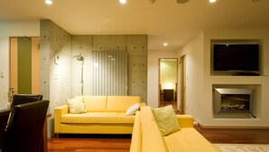 A modern living room with a yellow sofa, a flat-screen TV mounted above a fireplace, and a dining area with chairs and a table. - Holiday Niseko Cecuko (Kutchan)