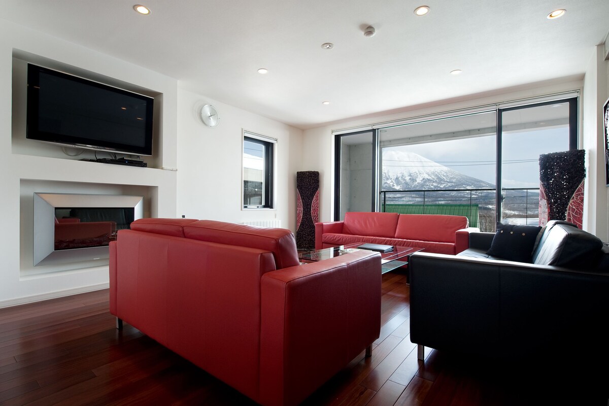 A modern living room with red sofas, a flat-screen TV, and a fireplace.