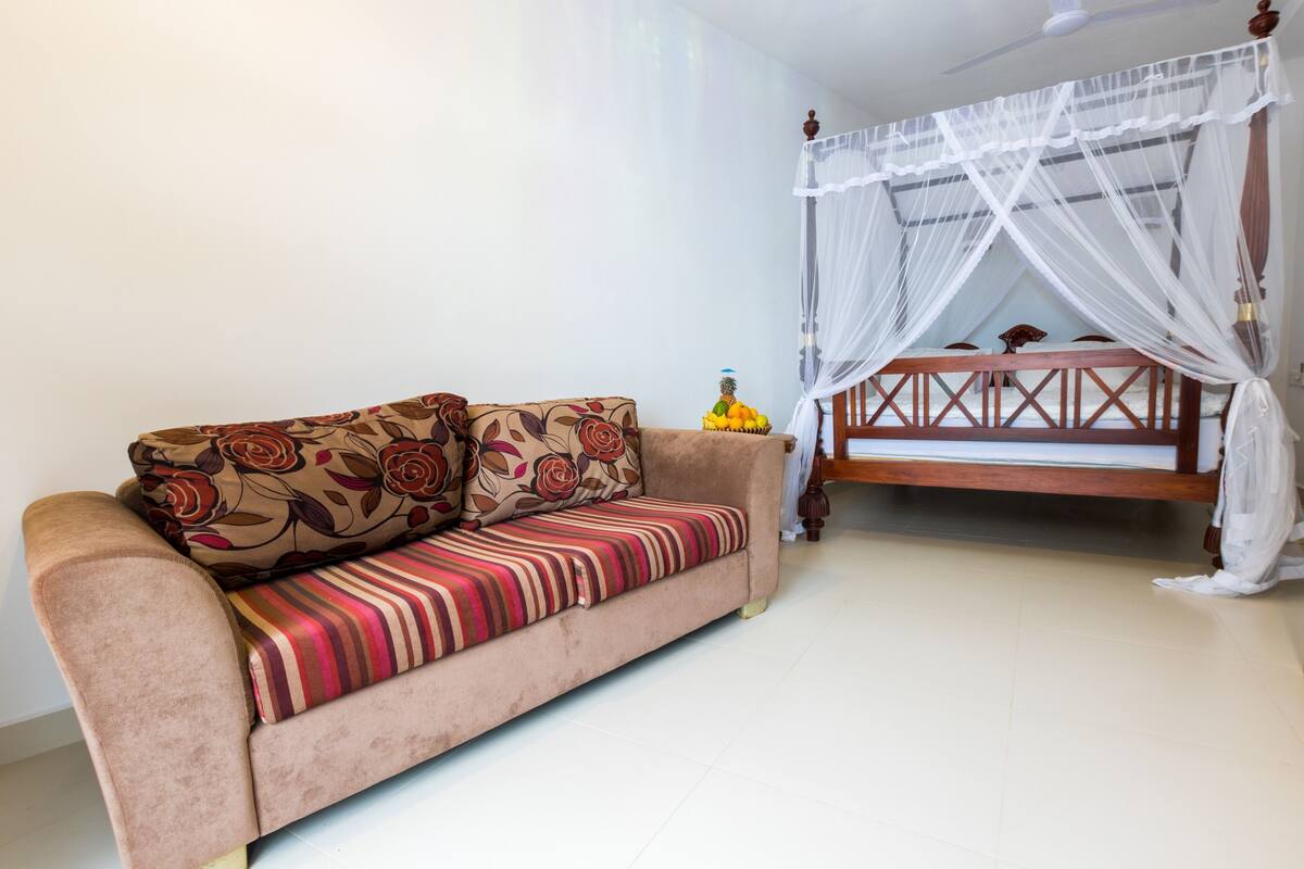 A room with a sofa, a bed with a canopy, and a small table with fruit.