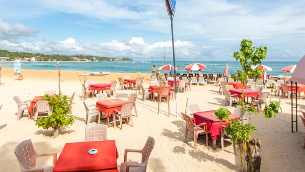 Un restaurante frente al mar con terraza, mesas rojas y sombrillas.