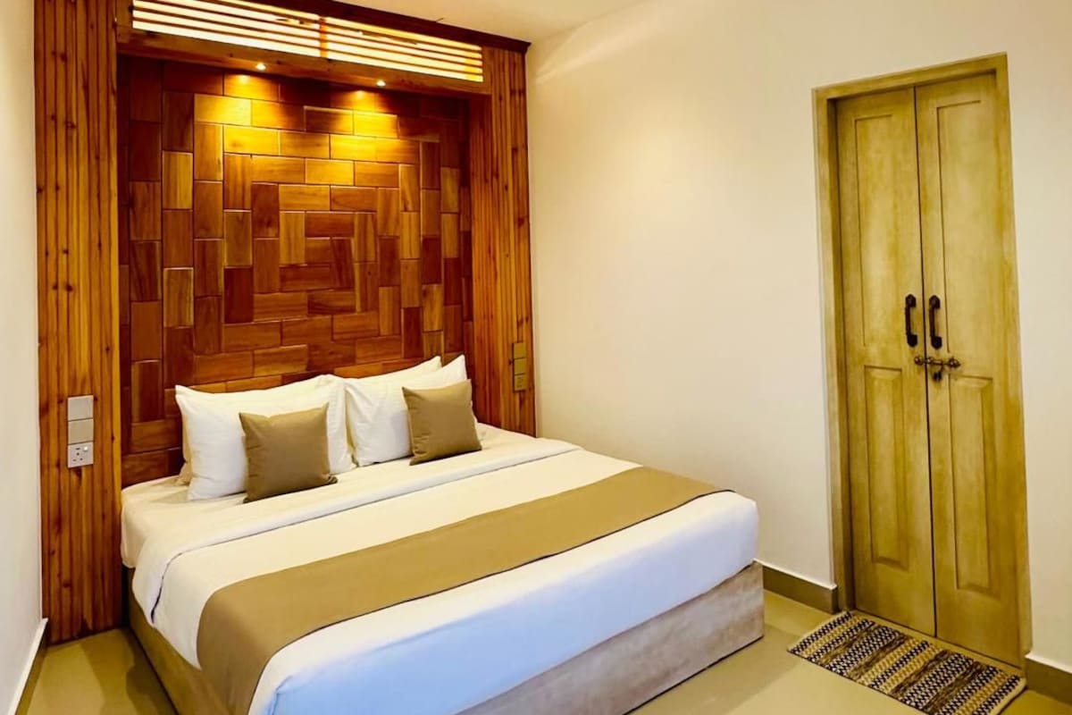 A modern bedroom with a wooden headboard, a large bed, a wooden door, and a ceiling vent.