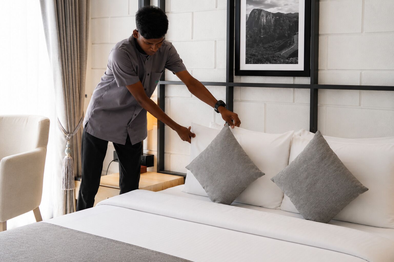 A person arranging pillows on a white sofa in a room with a white brick wall and a framed picture.