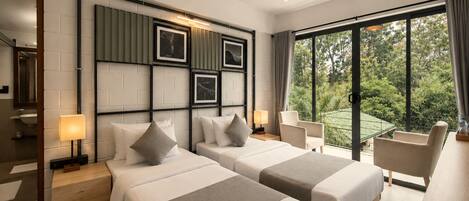 A hotel room with two beds, a large window with a view of greenery, a mirror, and a bedside table with a lamp.