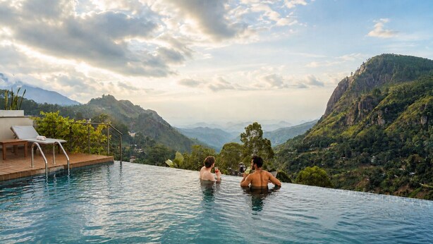 A pool with a view of mountains, a lounge chair, and a person holding a drink. - Onrock Boutique Hotel (Ella)