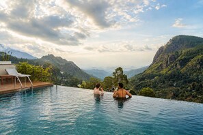 A pool with a view of mountains, a lounge chair, and a person holding a drink. - Onrock Boutique Hotel (Ella)