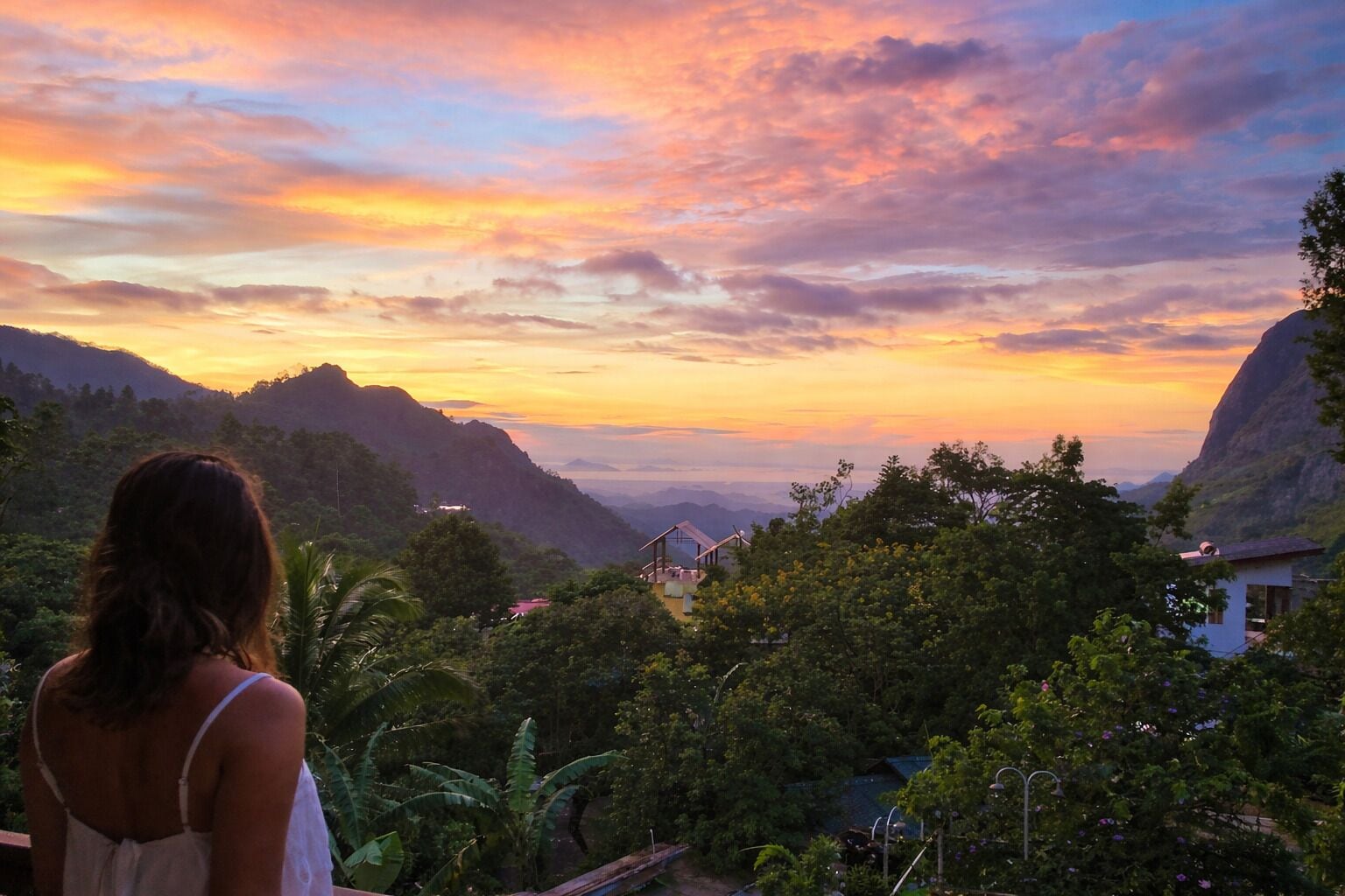 A woman overlooking a mountainous landscape with a sunset.